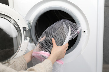 Wall Mural - Woman putting stylish sneakers into washing machine, closeup