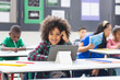 © WavebreakMediaMicro - Young biracial girl with curly hair using tablet in classroom