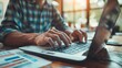 © admin_design - Closeup of a man's hands typing on a laptop keyboard. He is working on a project in a home office setting.