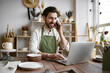 © sofiko14 - Mature Caucasian man in apron sits at table in ceramics shop and works with laptop. Experienced potter places online order while talking to customer over phone.