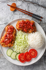 Canvas Print - Ayam geprek marinated chicken that's pounded, deep-fried and finished with a spicy sambal served with white rice, cucumber, tomato and cabbage closeup on the plate on the table. Vertical top view