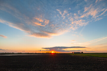 Wall Mural - The sun sets, still casting its colorful light on the clouds above the Dutch landscape