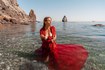 Wall Mural - A woman in a red dress is sitting in the water. The water is clear and the sky is blue.