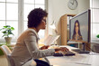 © Studio Romantic - Young African American woman accountant sitting at her office desk with business paperwork, having an online meeting with her colleague via a video call, looking at the computer screen, and smiling