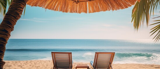 Wall Mural - Two lounges under an umbrella with palm leaves by the sea. Creative banner. Copyspace image