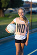 © Austockphoto - smiling young girl holding netball and wearing WD wing defence bib on netball court