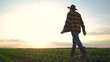 © maxximmm - The farmer works in the field of corn. agriculture a business concept. The silhouette farmer walk fields corn in the cornfield. farmer in a hat and boots walking corn lifestyle field