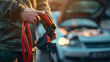 © john - Man holding red and black battery cable for charging the car. Car Repair and maintenance concept
