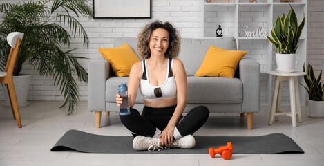 Poster - Happy sporty mature woman with dumbbells and bottle of water at home