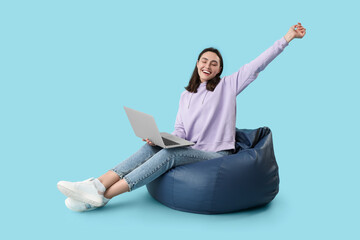 Wall Mural - Pretty young woman working with laptop while sitting on bean bag chair against blue background