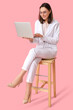 © Pixel-Shot - Young businesswoman with laptop sitting on chair against pink background