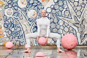 Wall Mural - Young hairless girl with alopecia in white futuristic suit dancing outdoor smoothly holding pink ball on abstract mosaic Soviet background, symbolizes self expression and cultural identity