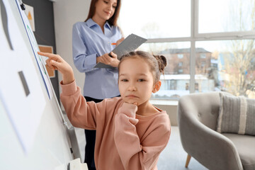 Wall Mural - Thoughtful little girl pointing at happy smile on board in psychologist's office