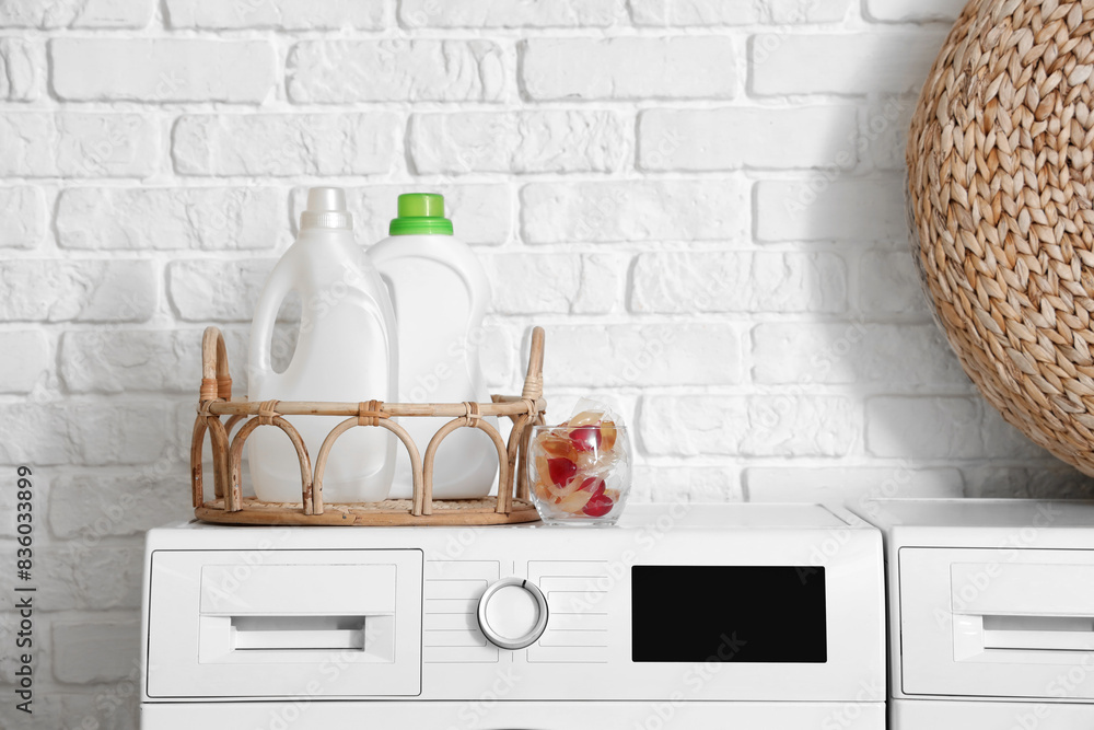Bottles and capsules of laundry detergent on washing machine, closeup