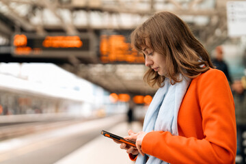 young woman traveler using phone waiting fortrain at railway station on platform