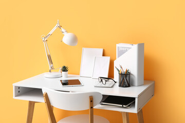 Wall Mural - Comfortable workplace with tablet computer, desk lamp and notebooks near orange wall