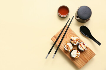 Wall Mural - Tasty sushi rolls with chopsticks, teapot and cup of tea on light yellow background