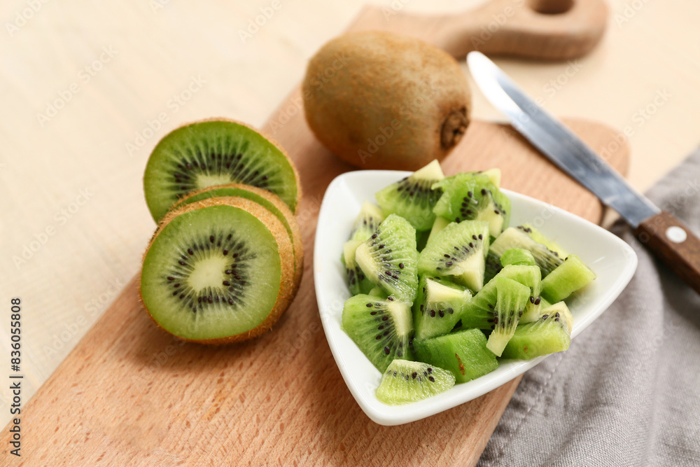 Board and bowl with fresh kiwi on wooden background