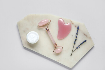 Stone board with jade roller, gua sha, cosmetic cream and lavender on grey background