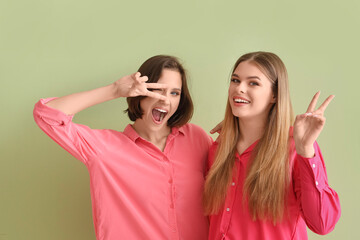 Wall Mural - Female friends showing victory gesture on green background