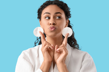 Wall Mural - Young African-American woman with cotton pads blowing kiss on blue background, closeup