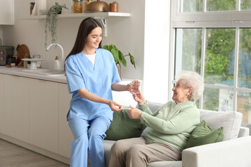 Wall Mural - Young nurse giving pills and glass of water to senior woman in kitchen