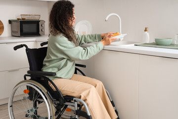 Poster - Young African-American woman in wheelchair washing dishes at home