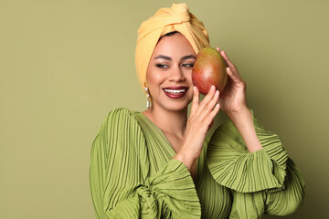 Beautiful African-American woman with fresh mango on green background