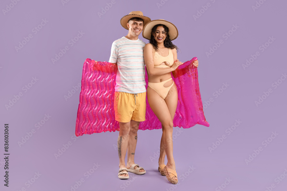 Happy young couple with inflatable mattress on lilac background