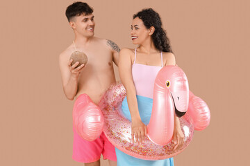 Wall Mural - Happy young couple with coconut and inflatable ring in shape of flamingo on brown background