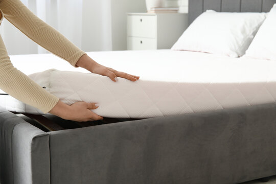 Woman putting soft orthopedic mattress on bed at home, closeup