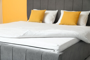 Poster - New orthopedic mattress with blanket on stylish bed near yellow wall in room, closeup