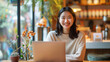 © aekkorn - Happy young Asian girl working at a cozy coffee shop with a laptop.