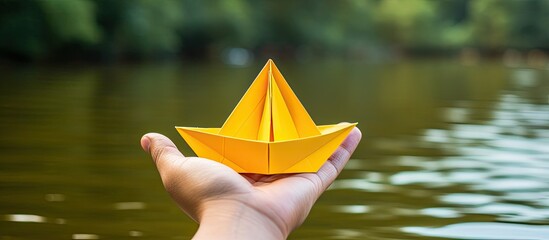 Wall Mural - A top-view image showing female hands folding an origami boat on a yellow background with copy space.