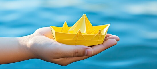 Wall Mural - A top-view image showing female hands folding an origami boat on a yellow background with copy space.