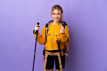 Teenager girl with backpack and trekking poles over isolated purple background making money gesture