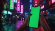 © Mrzproducer - hand holding a green screen phone in front of a blurred background of a busy street at night