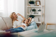 © SHOTPRIME STUDIO - Mother and child bonding on couch with laptop and bookshelf in cozy living room setting