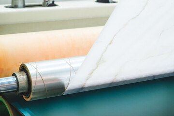 Poster - A roll of white paper is being fed through a machine. The machine is in a factory setting