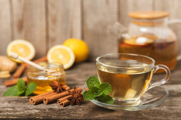 Wall Mural - Fragrant hot tea with cinnamon stick and anise on a textured wooden background. A cup of hot tea with honey, lemon, mint and apples. Spicy tea with spices. Immunity tea. Health concept.Copy space.