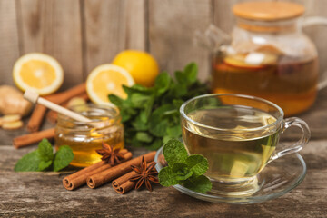 Wall Mural - Fragrant hot tea with cinnamon stick and anise on a textured wooden background. A cup of hot tea with honey, lemon, mint and apples. Spicy tea with spices. Immunity tea. Health concept.Copy space.