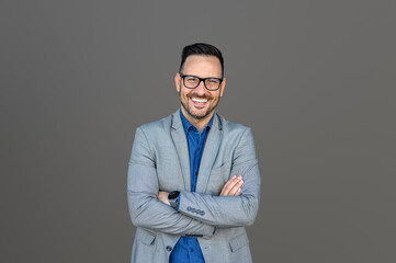 Wall Mural - Portrait of inspired male CEO in eyeglasses and with arms crossed posing isolated on gray background