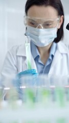 woman scientist with protective gloves and glasses examining lab tube with a green fluid. microbiolo