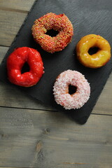 Wall Mural - Four appetizing glazed doughnuts: red, white, yellow with sprinkles on a gray background, top view. National desserts