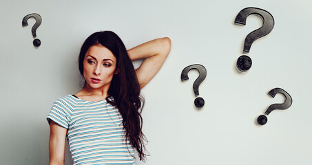 Wall Mural - Serious angry woman wants understanding looking down in casual clothing with question signs around on blue studio background with empty copy space. Closeup