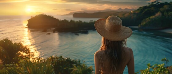 Wall Mural - A young woman, adorned with a hat, overlooks a calm sea in a lush tropical setting. The wide shot captures the serene vibe, bathed in the warm glow of golden hour light.
