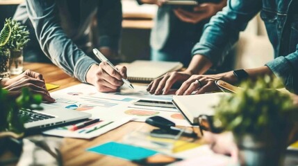 Wall Mural - Group of people collaborating on a project with charts, graphs, and laptops on a desk in a well-lit office environment.