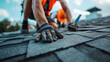 © Hound - Roofer worker in special protective work wear and gloves, installing asphalt or bitumen shingle on top of the new roof under construction residential building