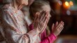 © NEW - An elderly woman and a young girl clasping hands in prayer together, displaying a touching moment of intergenerational spirituality.