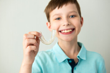 child boy hold in hand invisible transparent aligners, invisalign bracer smile isolated on light gra